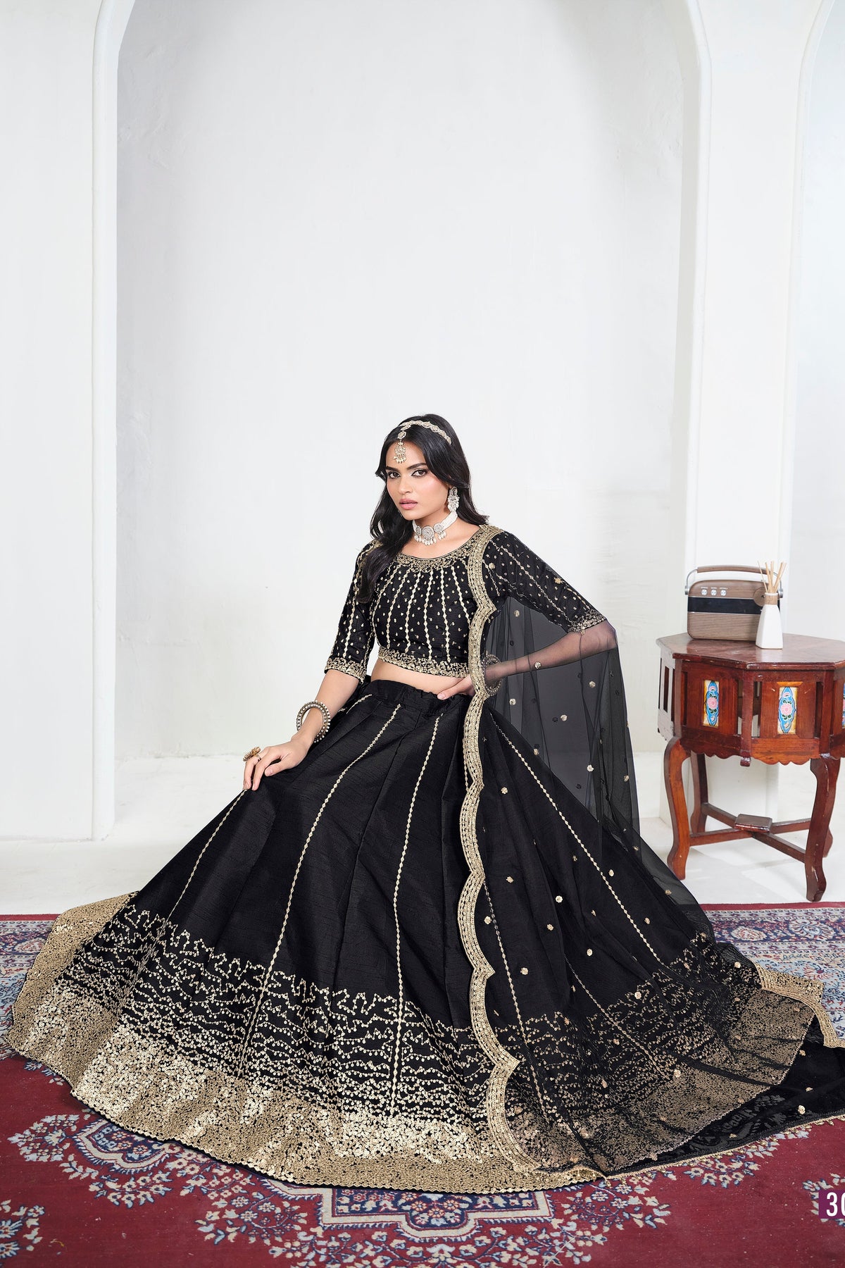 Alternate view of a black embroidered lehenga with mirror work on the lehenga skirt, seated pose, full outfit visible. All-over mirror work.