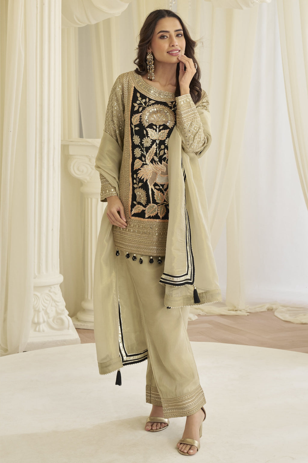 Model in the beige palazzo salwar kameez with the dupatta draped forward over both arms.