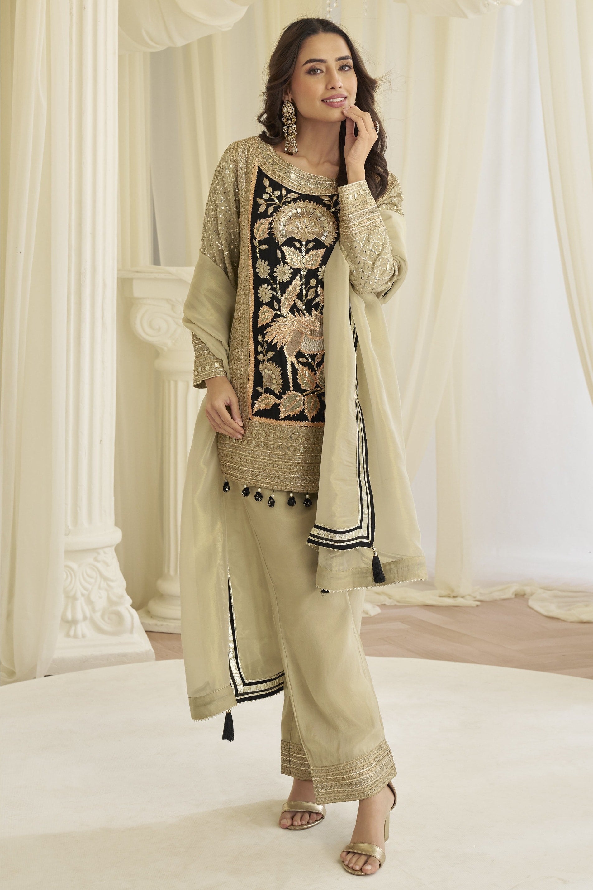 Model in the beige palazzo salwar kameez with the dupatta draped forward over both arms.