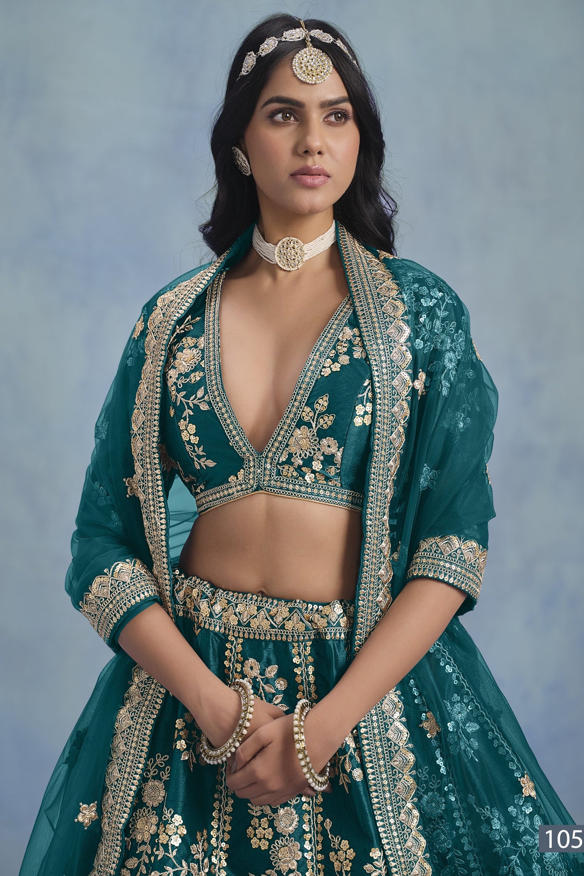 A waist-up front view shows a woman in a Teal blue embroidered lehenga choli for reception with a V-neck embroidered blouse and net dupatta.