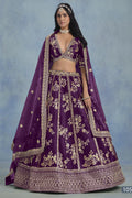 A woman in a full-length front view wears a purple embroidered lehenga choli for reception with floral work and net dupatta on a blue studio backdrop.