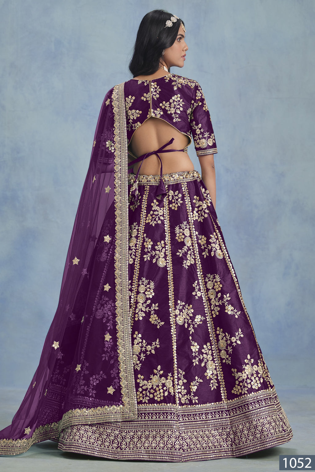 A back view of a woman in a purple embroidered lehenga choli for reception shows the open-back blouse, embroidered skirt and net dupatta.