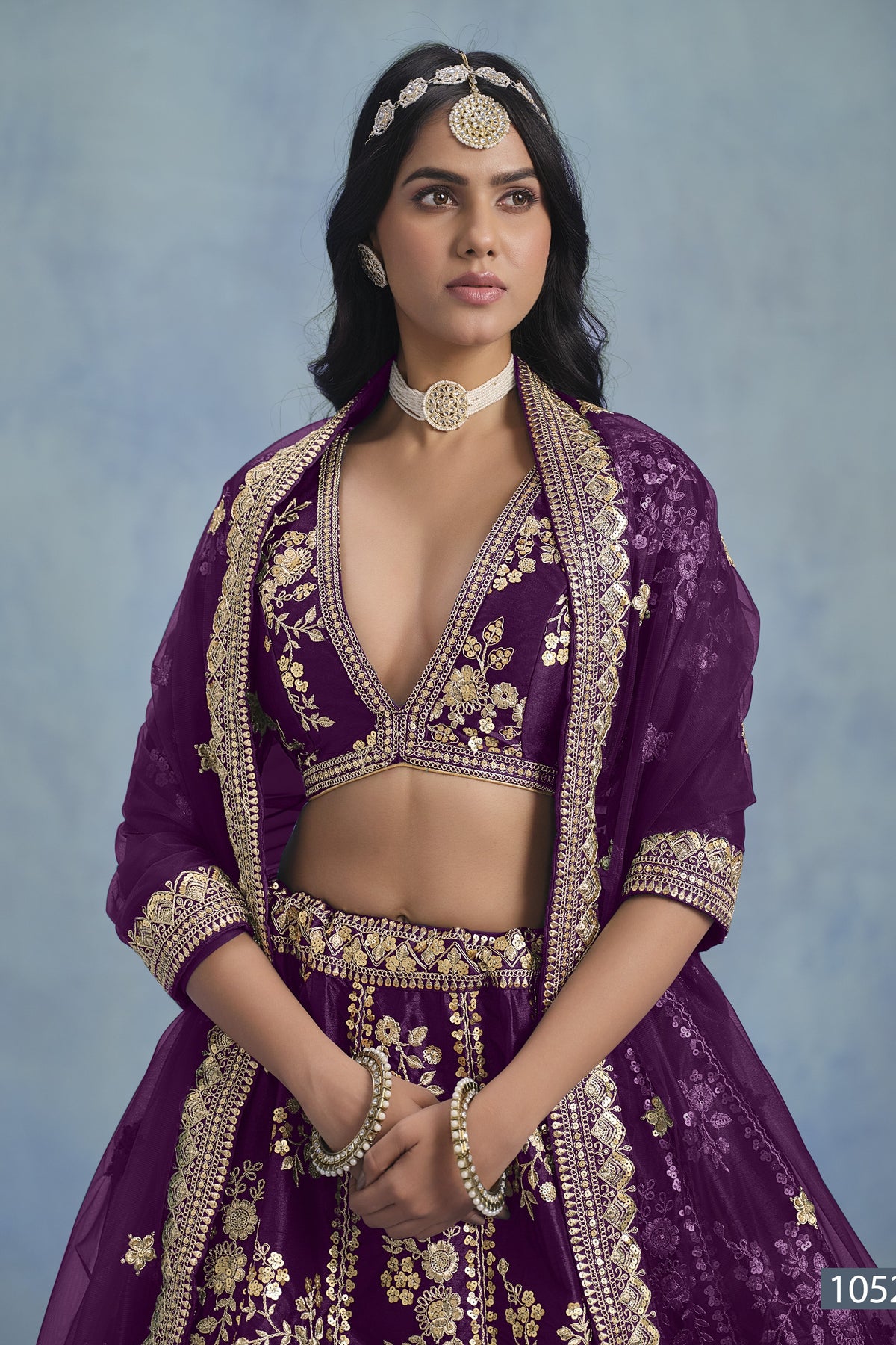 A waist-up front view shows a woman in a purple embroidered lehenga choli for reception with a V-neck embroidered blouse and net dupatta.