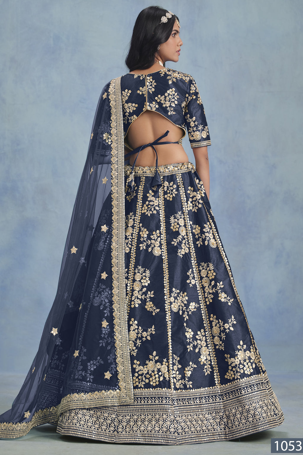 A back view of a woman in a navy blue embroidered lehenga choli for reception shows the open-back blouse, embroidered skirt and net dupatta.