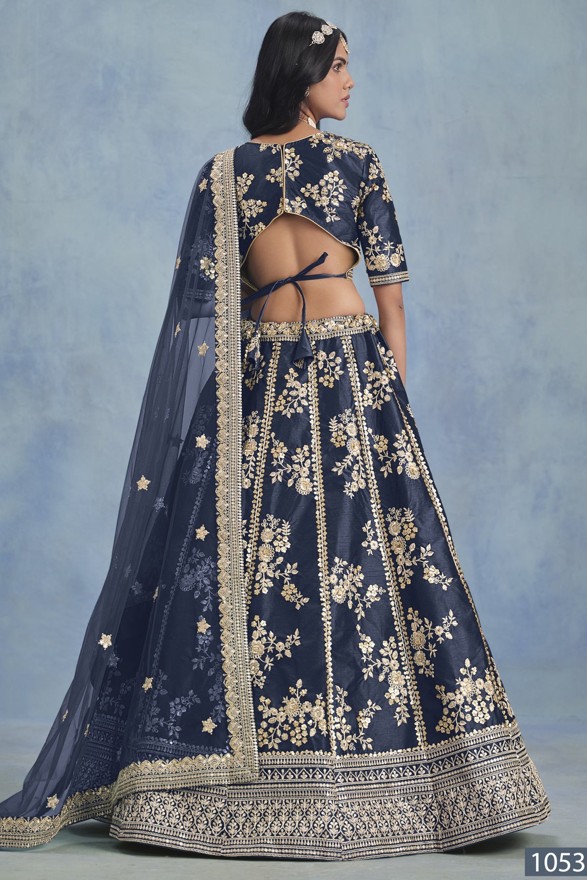 A back view of a woman in a navy blue embroidered lehenga choli for reception shows the open-back blouse, embroidered skirt and net dupatta.