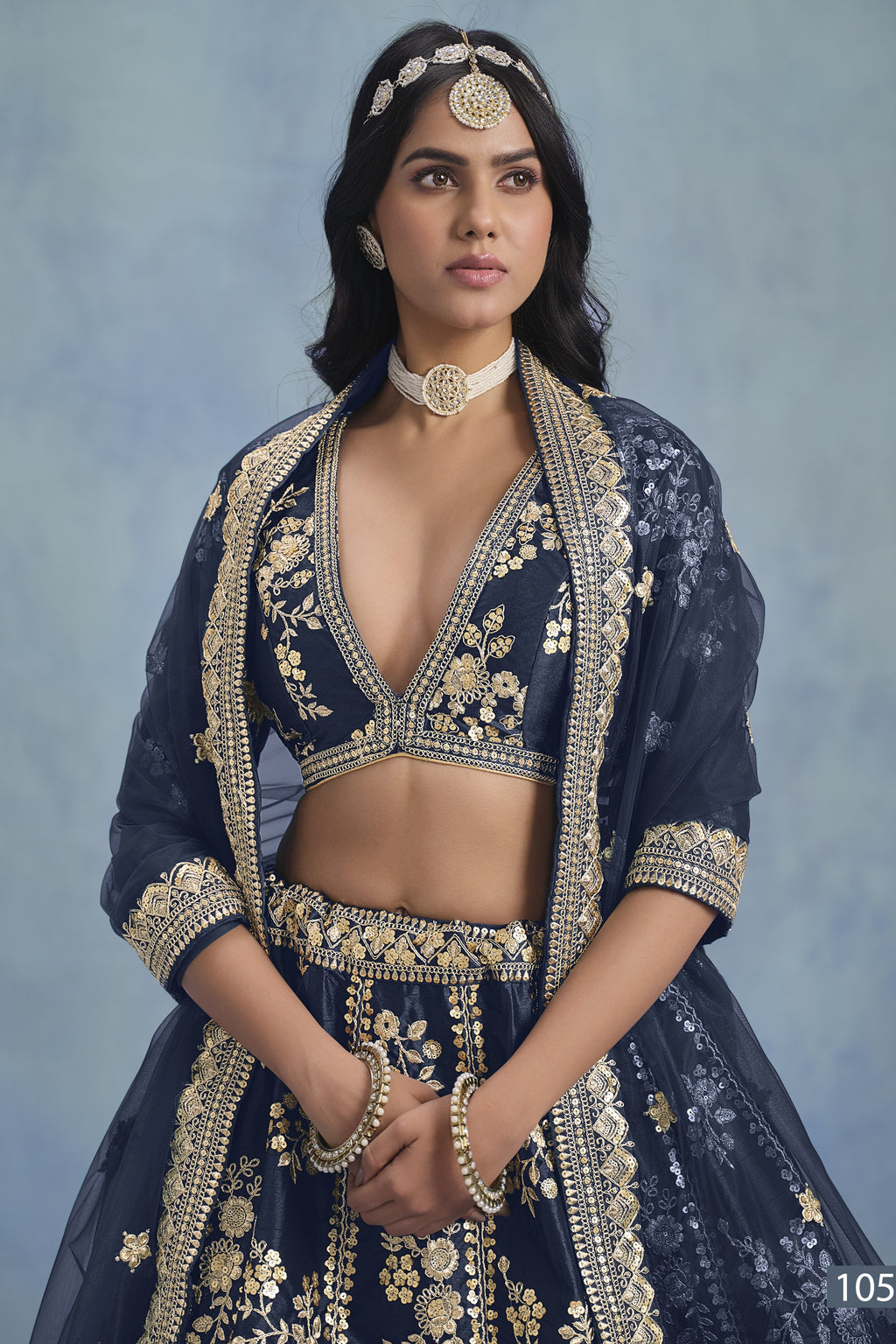 A waist-up front view shows a woman in a navy blue embroidered lehenga choli for reception with a V-neck embroidered blouse and net dupatta.