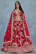 A woman in a full-length front view wears a red embroidered lehenga choli for party with floral work and net dupatta on a blue studio backdrop.