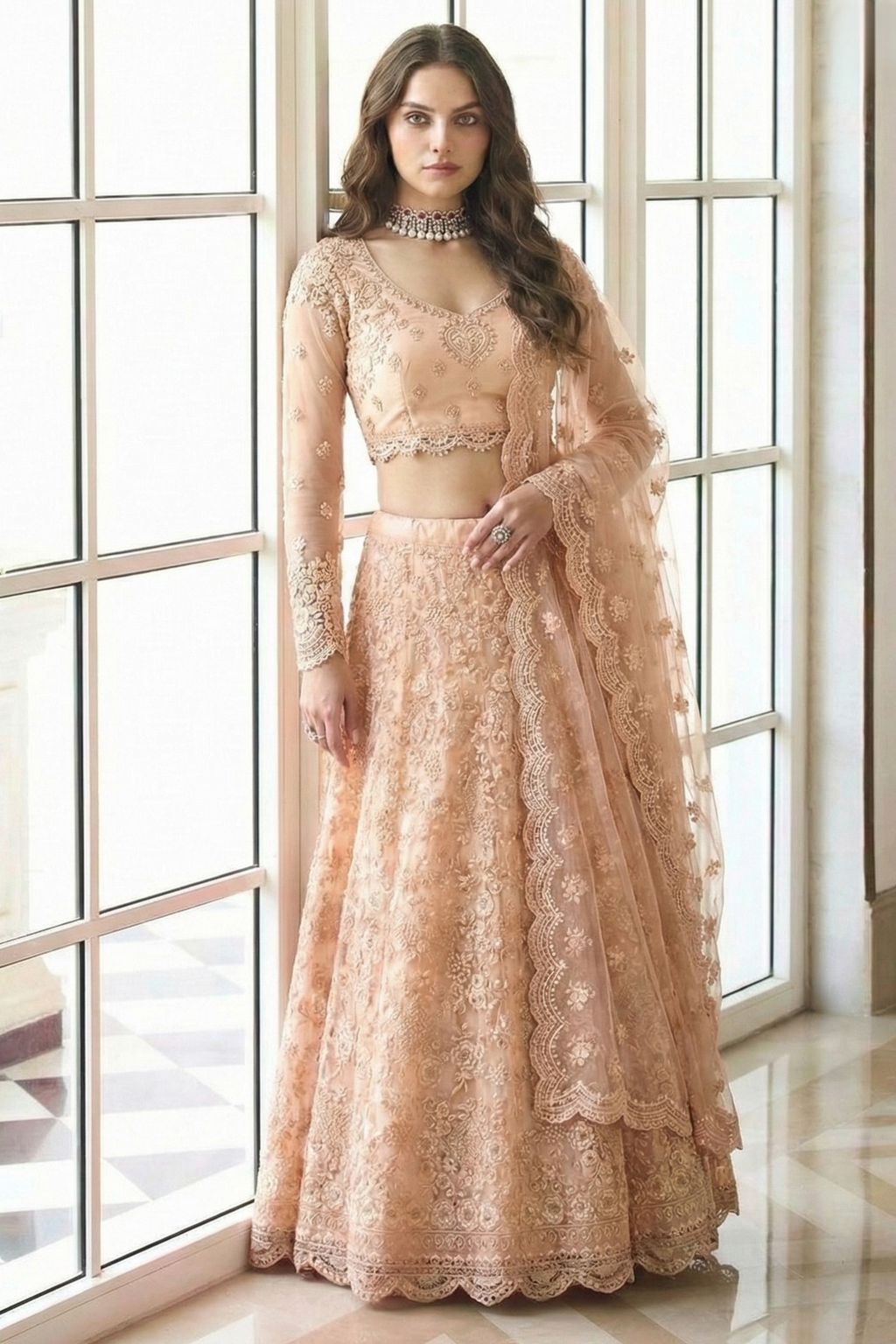 Model wearing a peach net lehenga choli with long sheer sleeves, V neckline and scalloped dupatta, styled with a choker — a delicate reception lehenga with dori, thread and stone work.