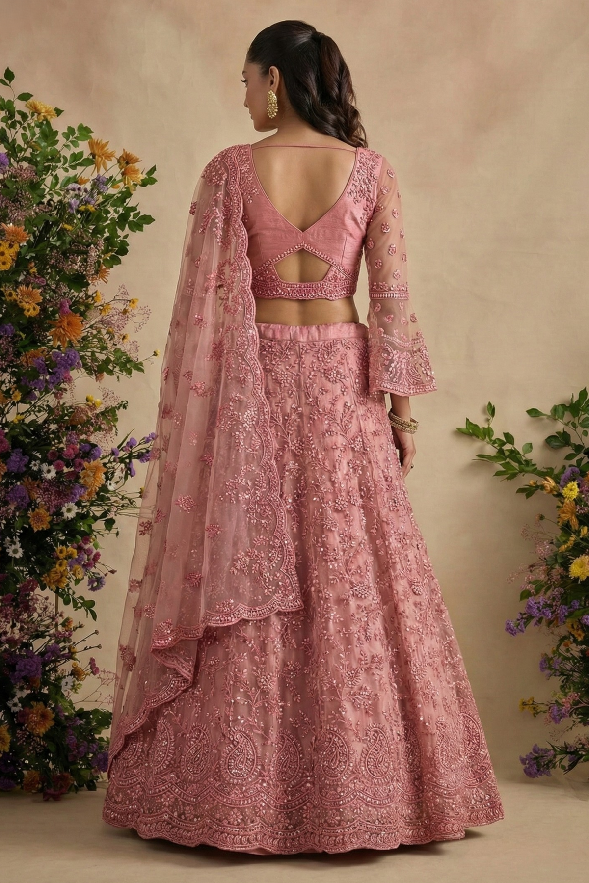 Back view of the dusty pink blouse with open back and crisscross dori ties, sheer bell sleeves — a delicate reception lehenga in embroidered pink net.
