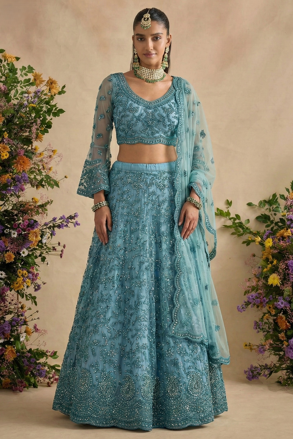 Model in a teal net lehenga choli with long sheer sleeves, V neckline and scalloped dupatta, wearing a maang tikka — a graceful long sleeve sangeet lehenga with stone work.