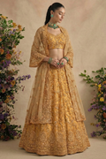 Model wearing a golden net lehenga choli with bell sleeves, V neckline and scalloped dupatta, styled with green jewellery — a radiant wedding guest lehenga with thread and stone work.