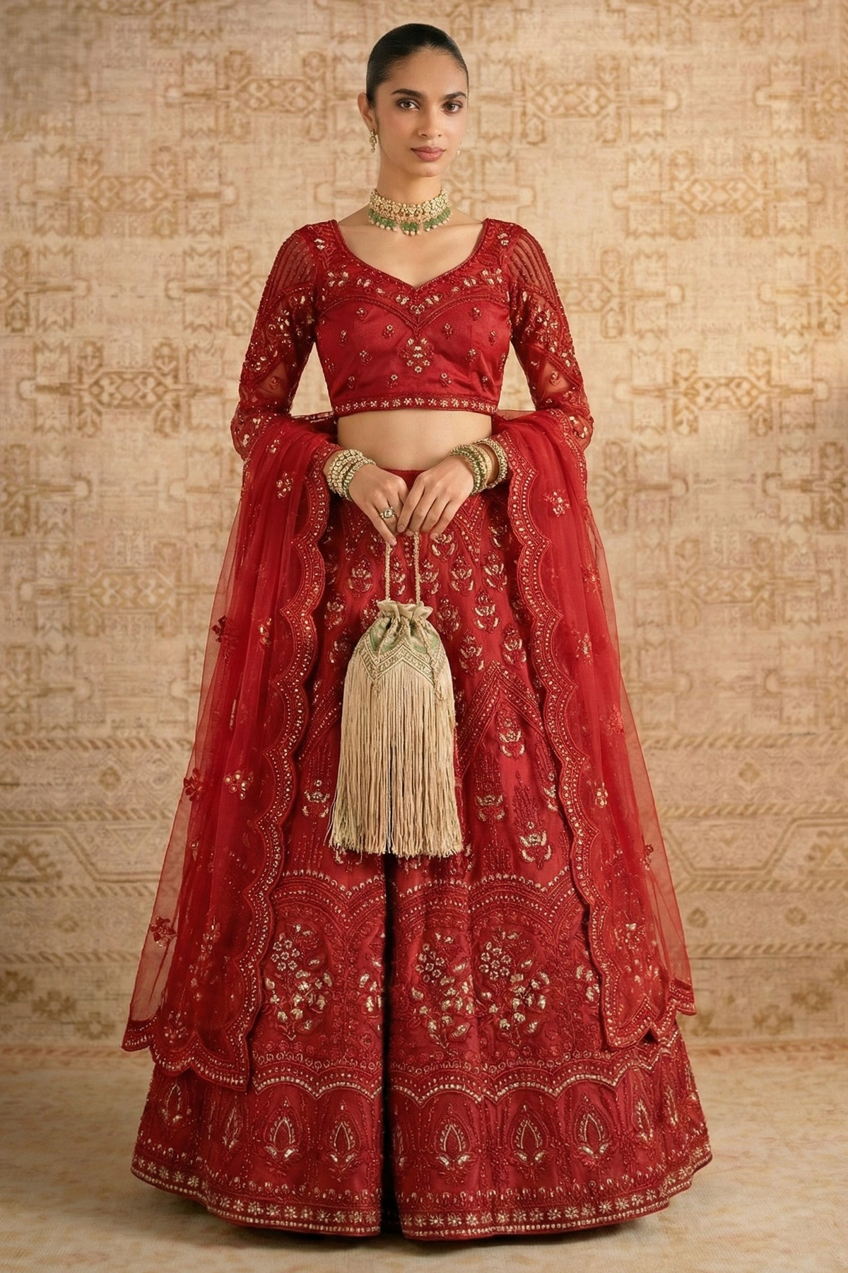 Model wearing a red net lehenga choli with long sheer embroidered sleeves, V neck blouse and potli bag — a striking long sleeve reception lehenga with gold hand embroidery.