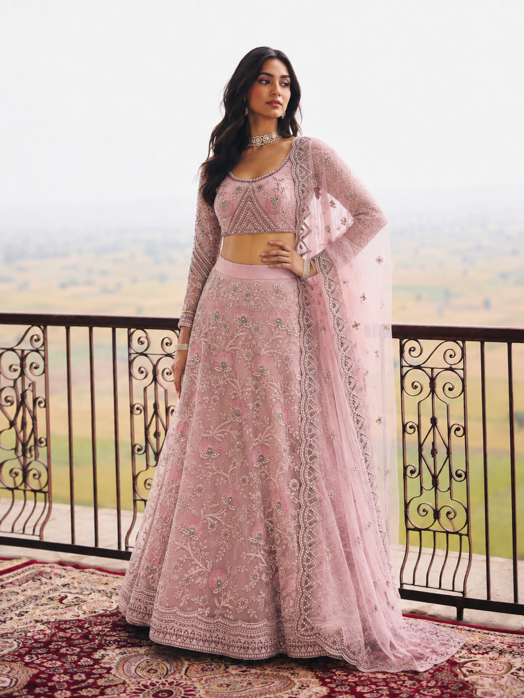 Woman wearing a baby pink lehenga for wedding guest with embroidery work, full sleeve round neck net choli, full-length front view.