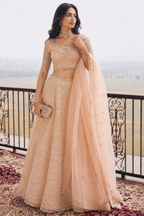 Lady standing in a peach lehenga choli and holding purse