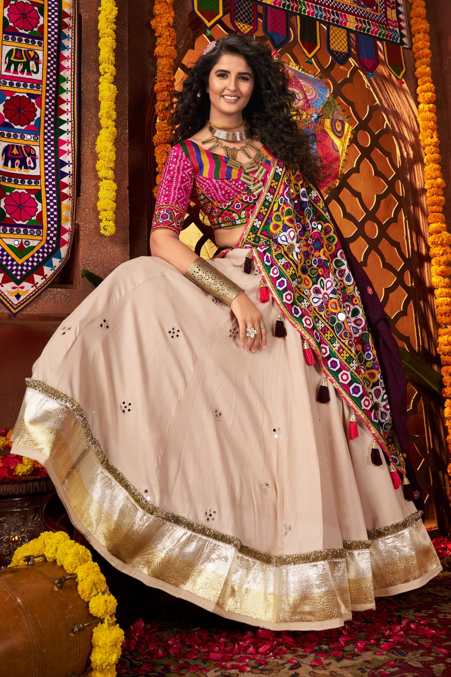 Woman in traditional attire standing in a decorated room with colorful decorations and patterns.