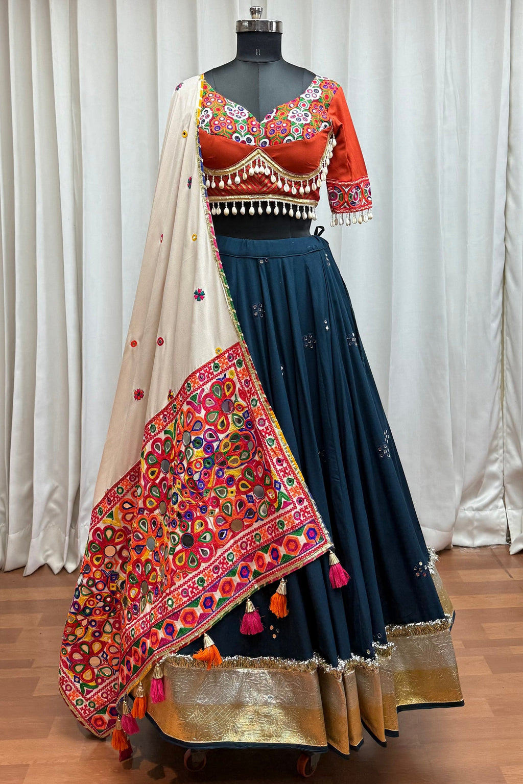 Traditional Indian outfit with a colorful blouse and navy blue skirt on a mannequin against a white curtain background.