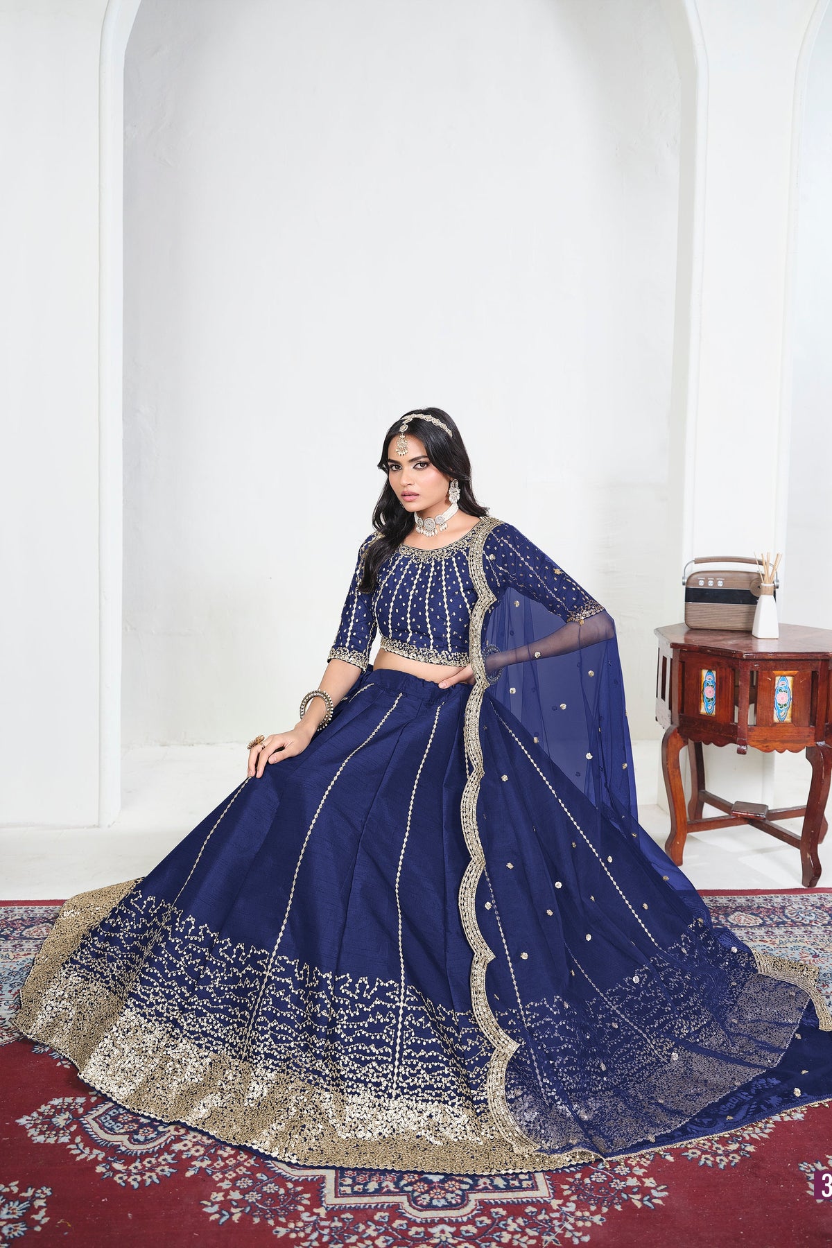 Alternate view of a navy blue mirror lehenga with mirror work on the lehenga skirt, seated pose, full outfit visible. All-over mirror work.