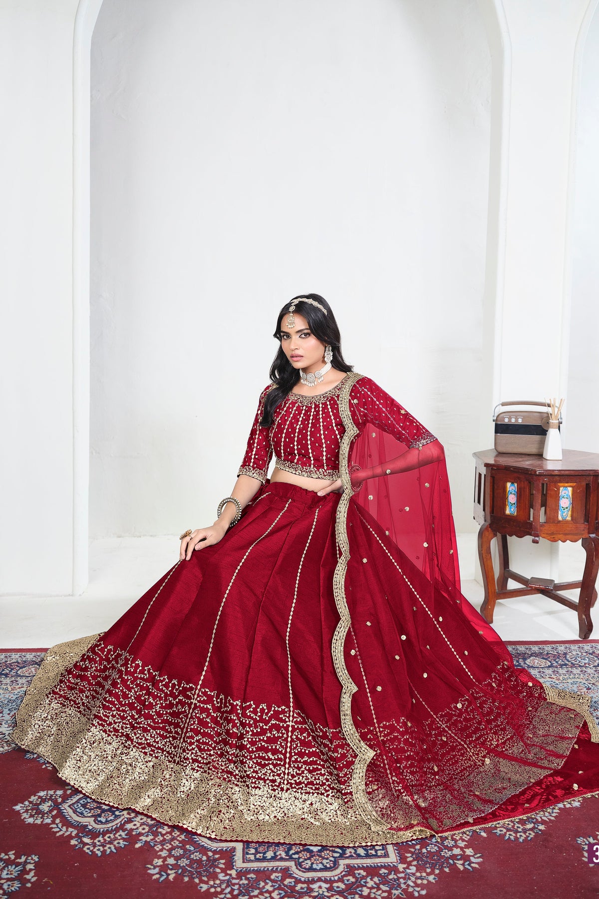 Alternate view of a red lehenga choli designs with mirror work on the lehenga skirt, seated pose, full outfit visible. All-over mirror work.