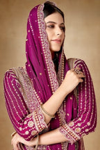 Woman wearing a traditional outfit with a purple dupatta against a beige background