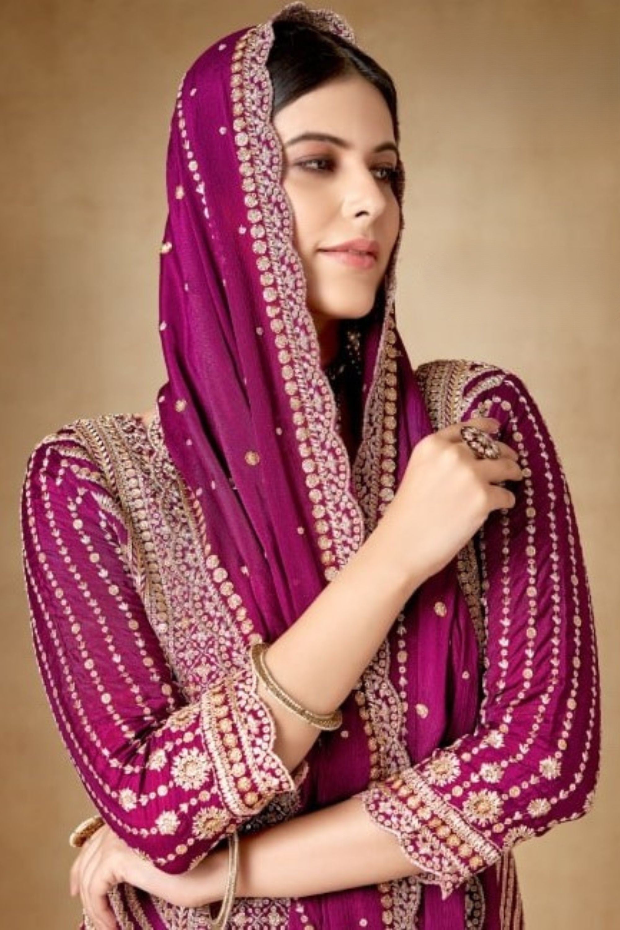 Woman wearing a traditional outfit with a purple dupatta against a beige background