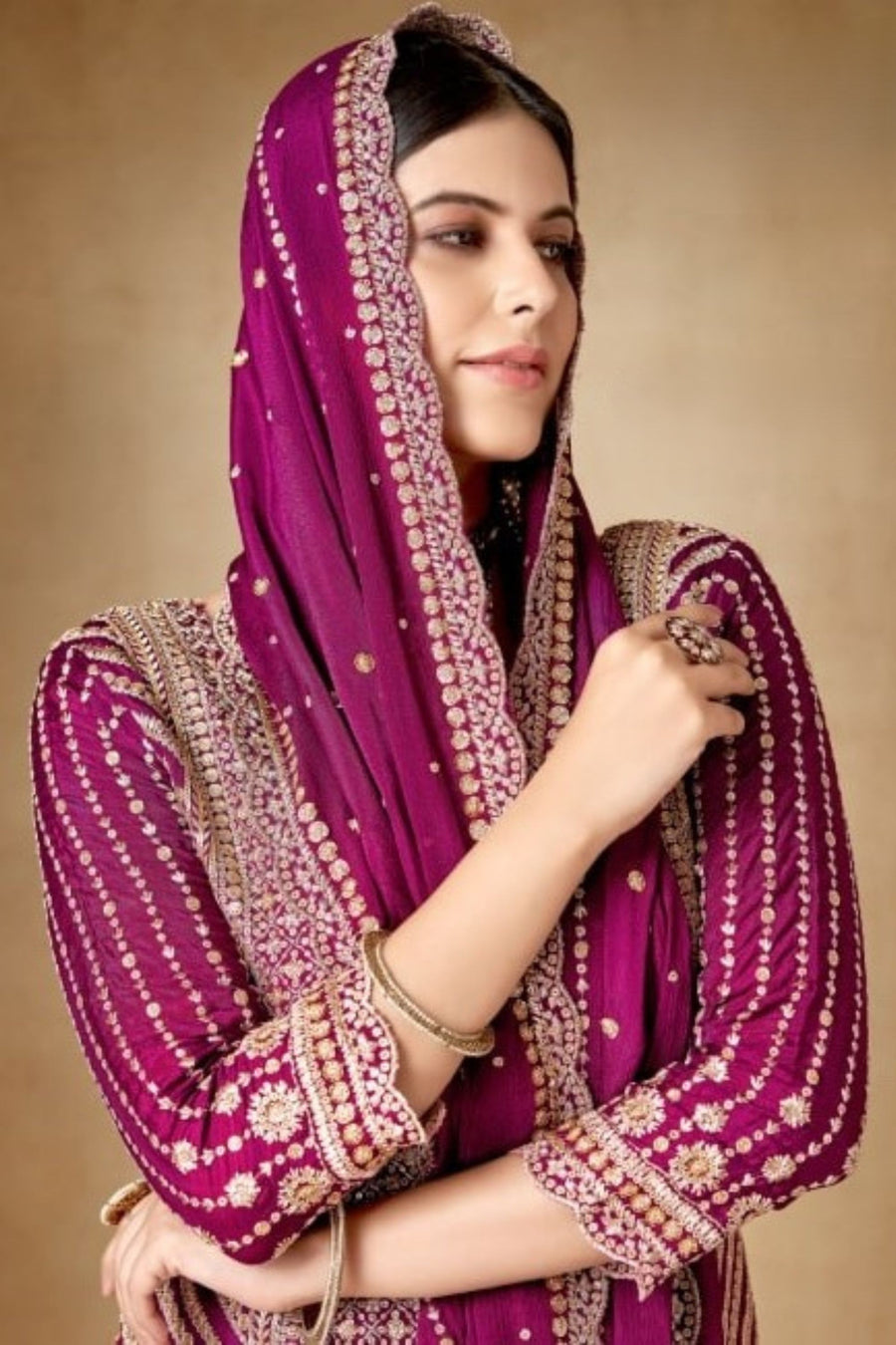 Woman wearing a traditional outfit with a purple dupatta against a beige background