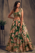 A full-length studio shot of a woman posing in an sleeveless embroidered floral lehenga choli green colour beside a potted plant.