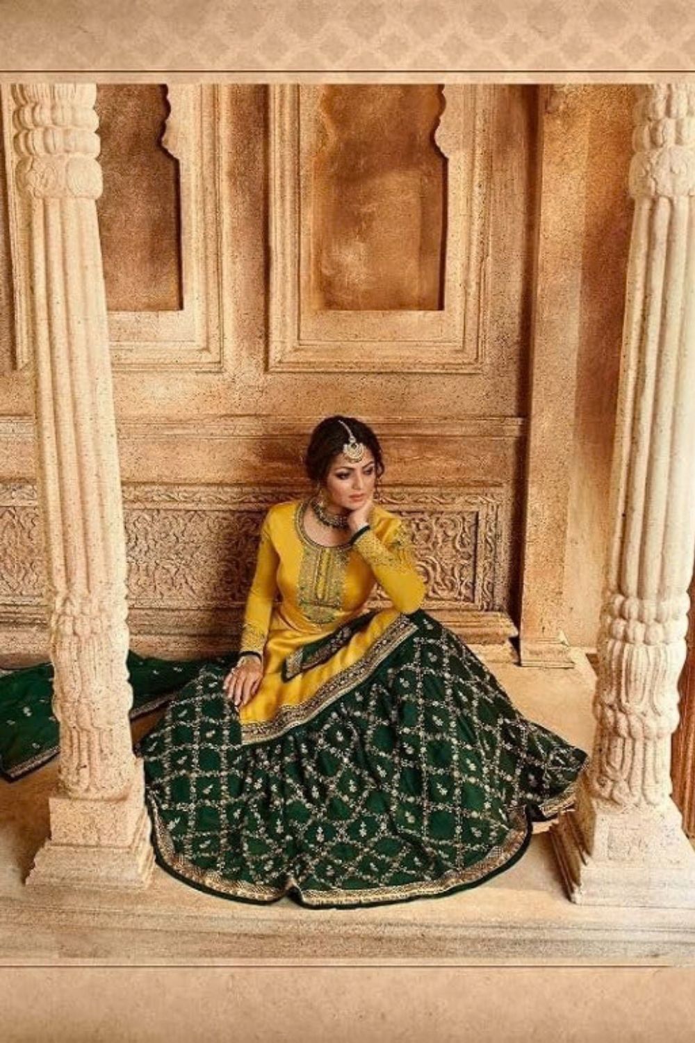 A portrait shows a seated woman in a yellow haldi outfit with a dark green embroidered skirt and traditional jewelry, presenting an elegant example of haldi outfits for guests against ornate sandstone architecture.