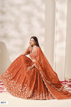 Woman wearing a rust orange lehenga for wedding in chinon silk with sequin and thread embroidery, embroidered blouse and dupatta, full-length seated front view.