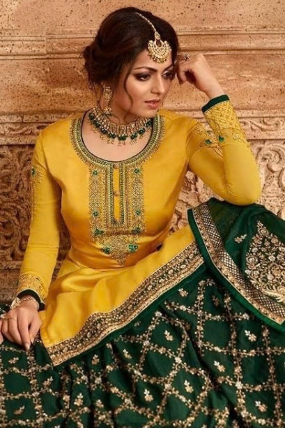 A seated three-quarter portrait shows a woman in a yellow embroidered haldi outfit with a dark green embellished skirt, offering inspiration for haldi dress for women