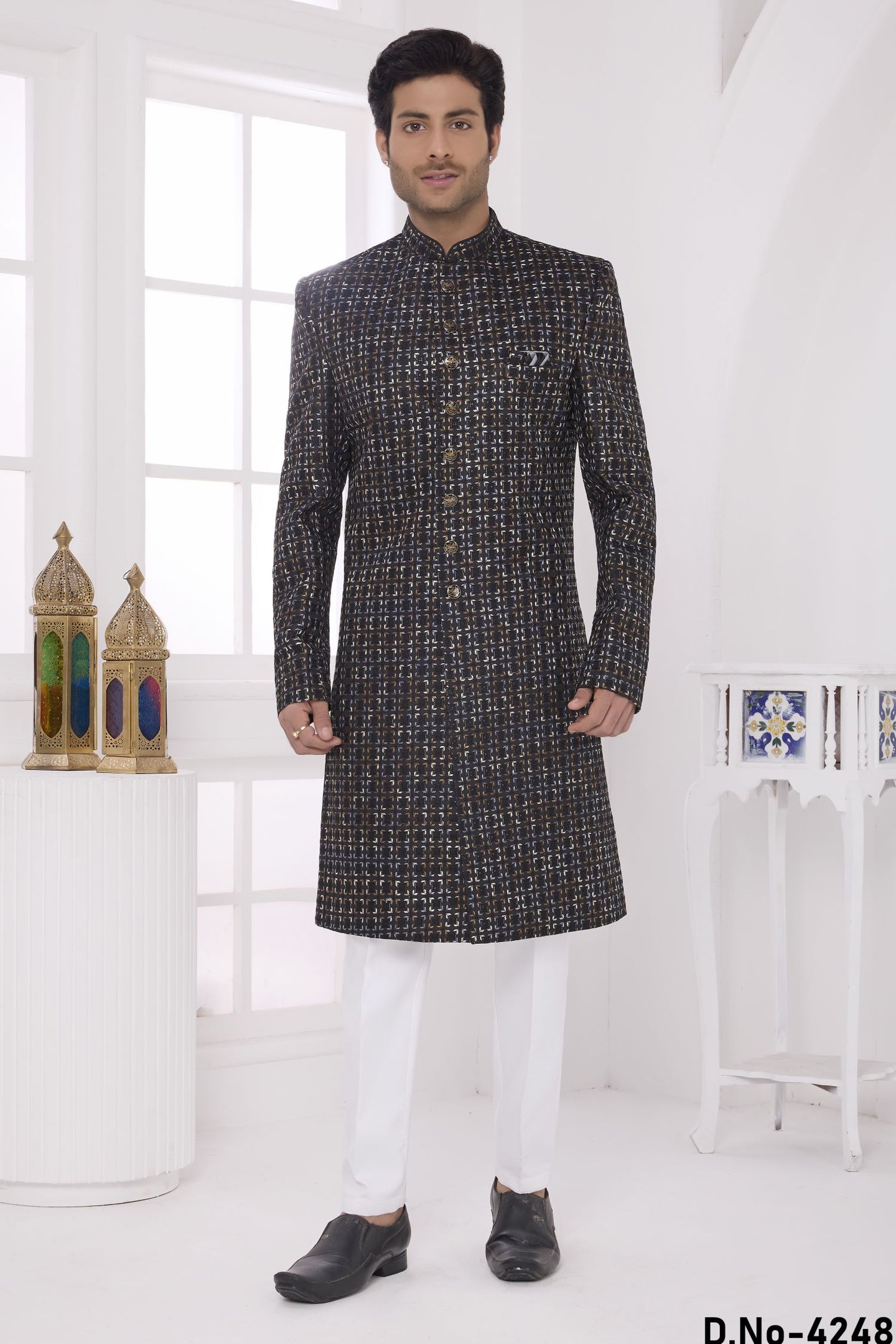 Man wearing a black and white patterned kurta with white pants in a minimalistic setting.