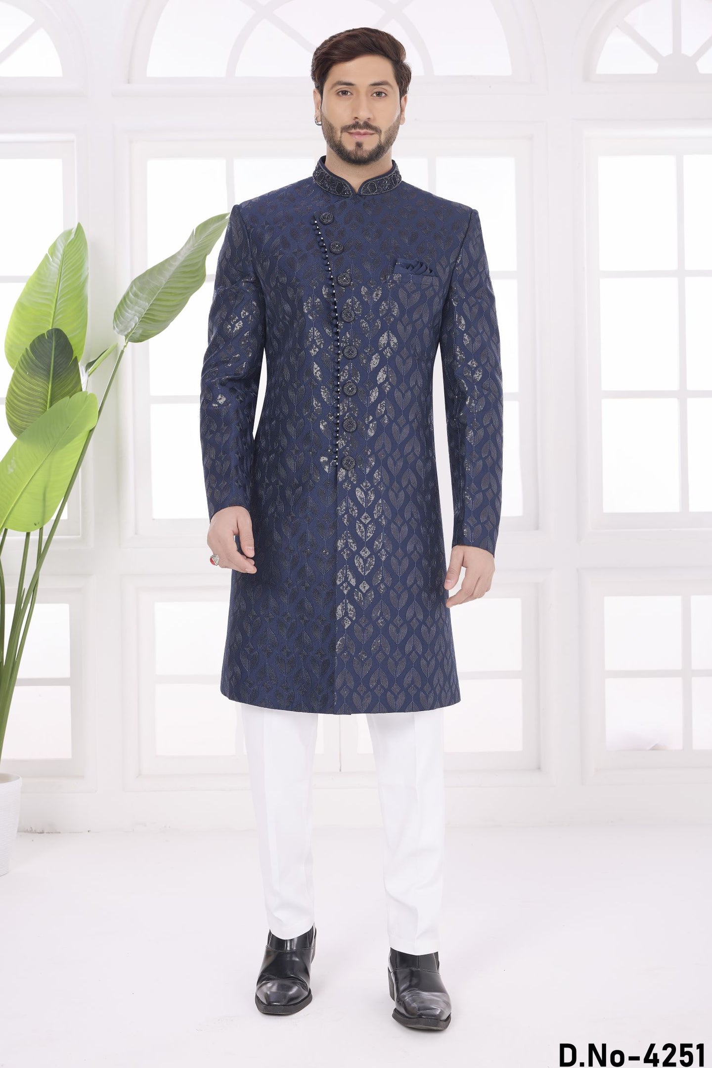 Man wearing a blue embroidered sherwani with white pants in a bright room.