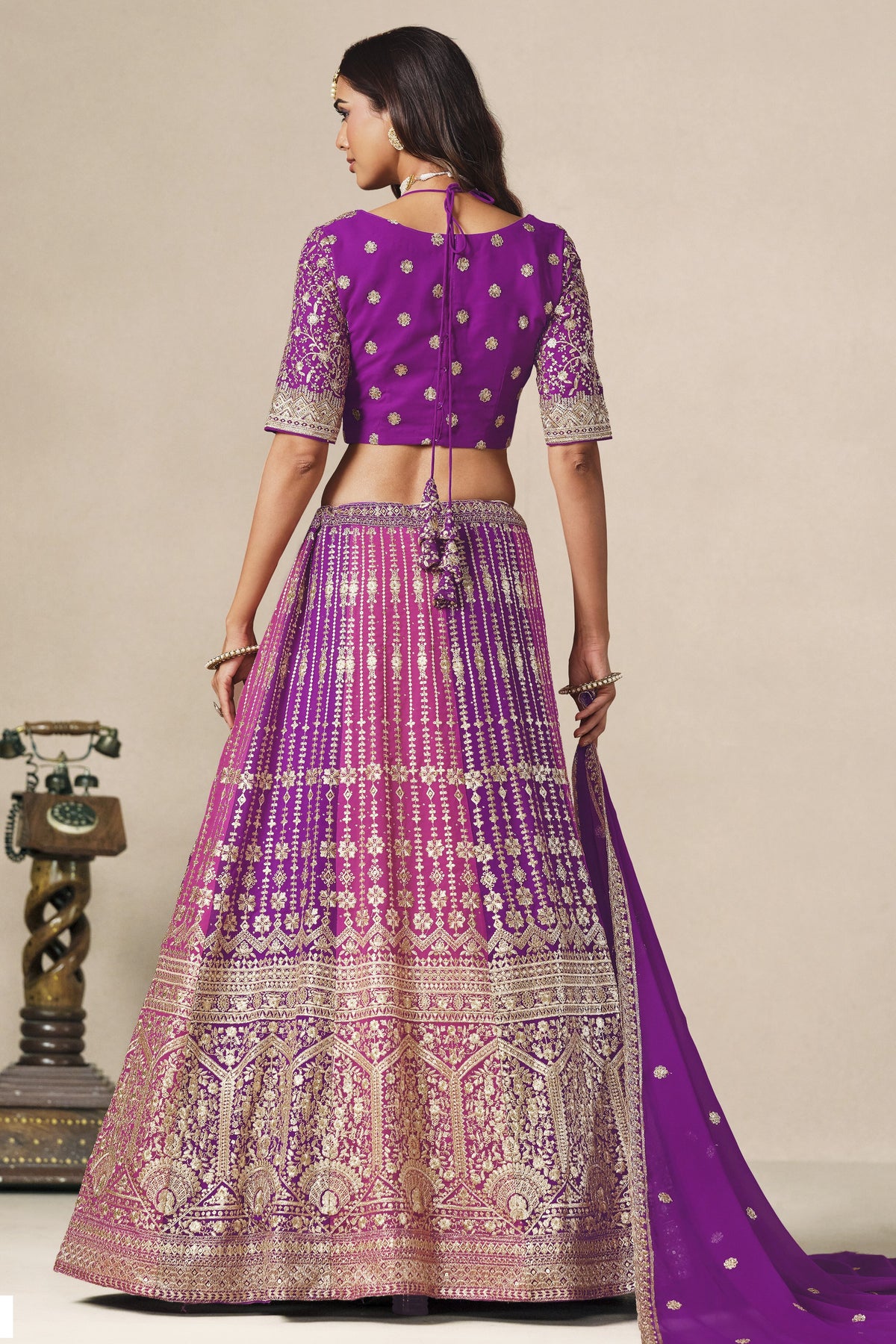 Full-length back view of a purple lehenga for wedding in georgette with an open cutout back blouse with dori tie and zari and sequin work.