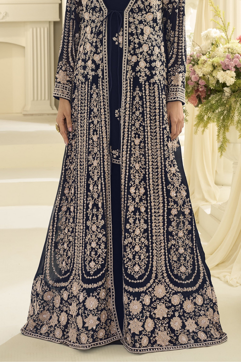 A navy blue floor-length anarkali with extensive embroidery, shown on a model in an elegant indoor setting.