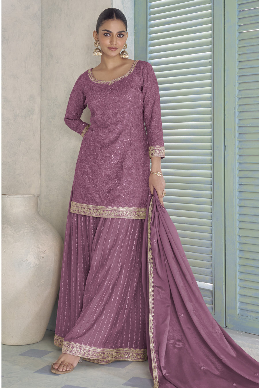 Woman wearing a mauve traditional outfit with a matching dupatta in a neutral setting.