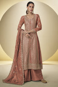 Woman wearing a traditional pink embroidered outfit with a dupatta on a beige background
