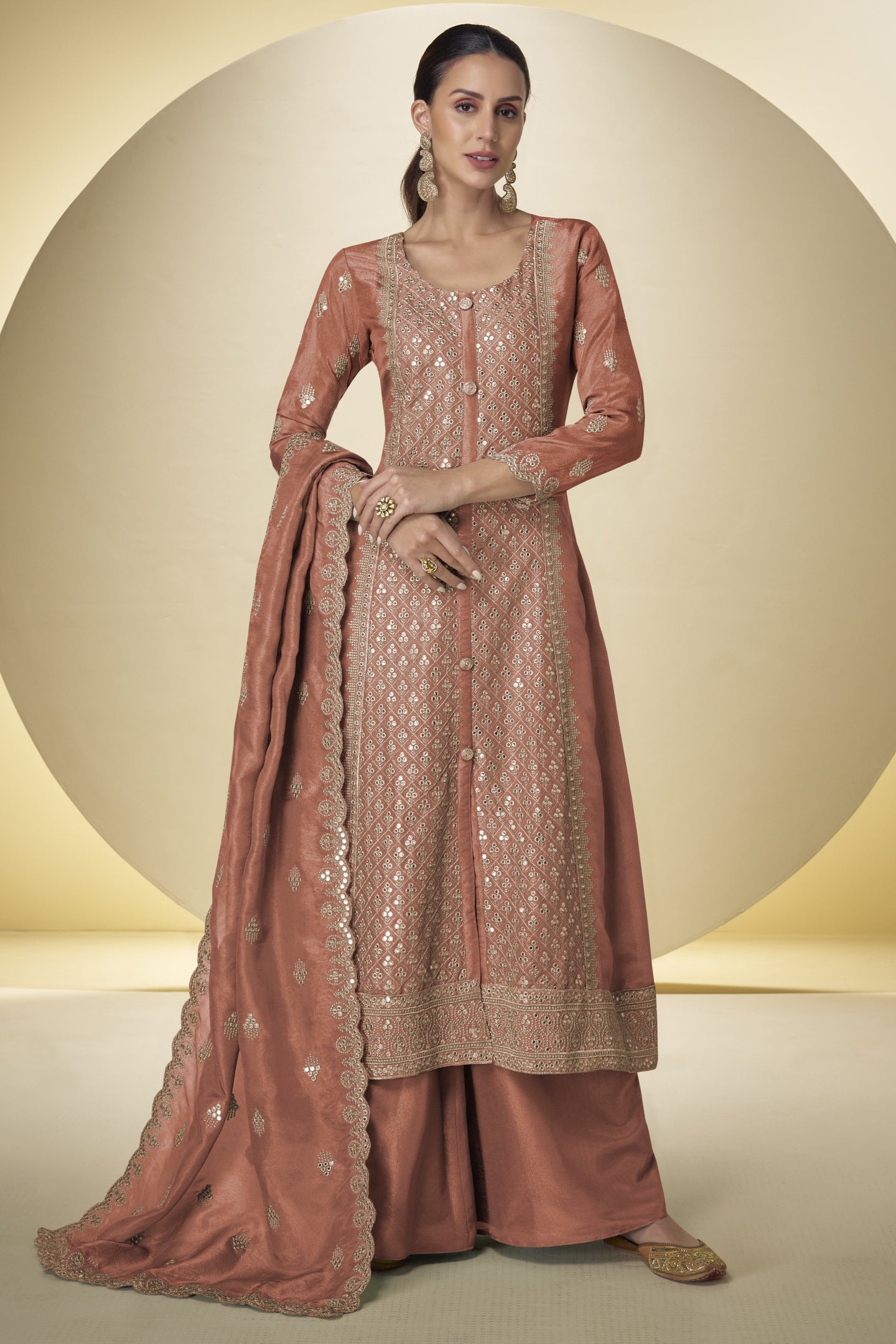 Woman wearing a traditional pink embroidered outfit with a dupatta on a beige background