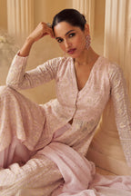 women seating in light pink anarkali suit near pillar