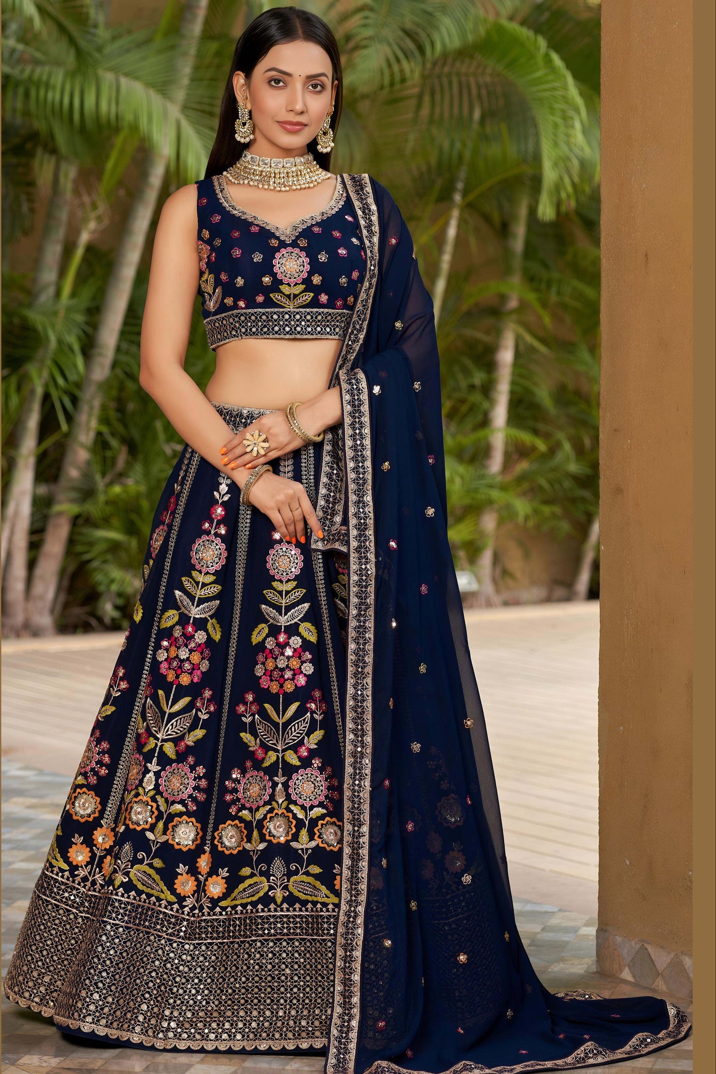 Woman wearing a navy blue embroidered lehenga with floral patterns in an outdoor setting.