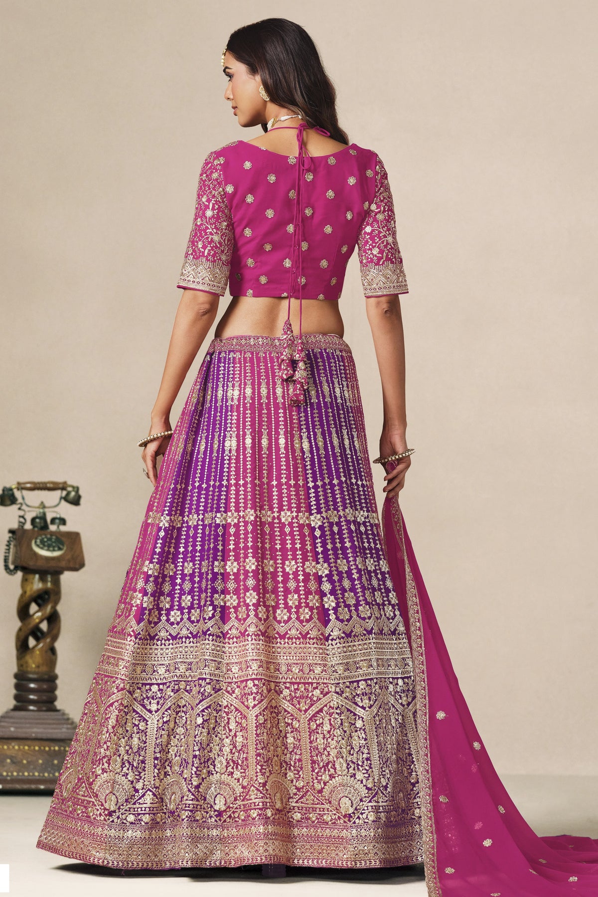 Full-length back view of a magenta lehenga for sangeet in georgette with an open cutout back blouse with dori tie and zari and sequin work.
