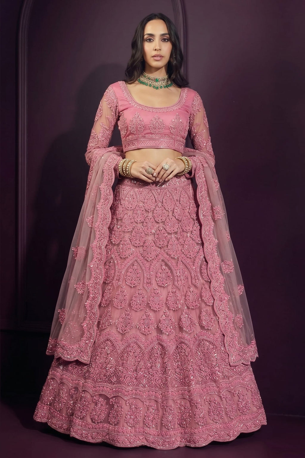 Coral pink engagement lehenga in net with hand-worked embroidery, long-sleeve blouse and dupatta draped over both shoulders.