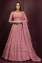 Front view of an indian lehenga choli in coral pink net with dense embroidery, long-sleeve choli and sheer dupatta on one shoulder.