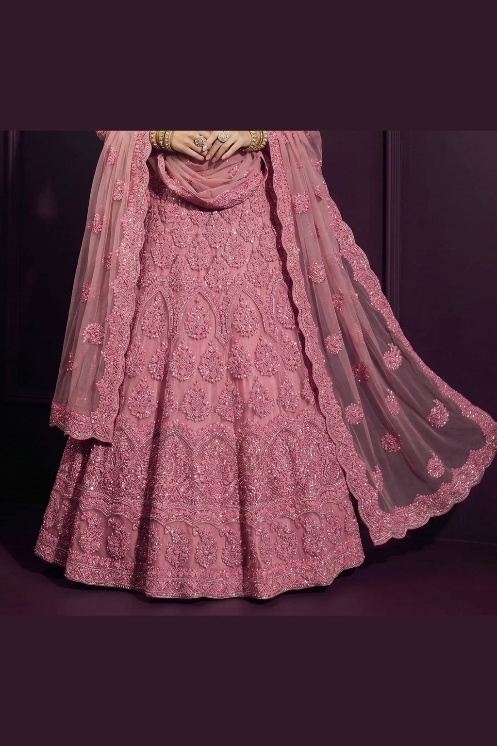 Waist-down close-up of the coral pink wedding guest lehenga skirt showing dense intricate hand embroidery across the net fabric.