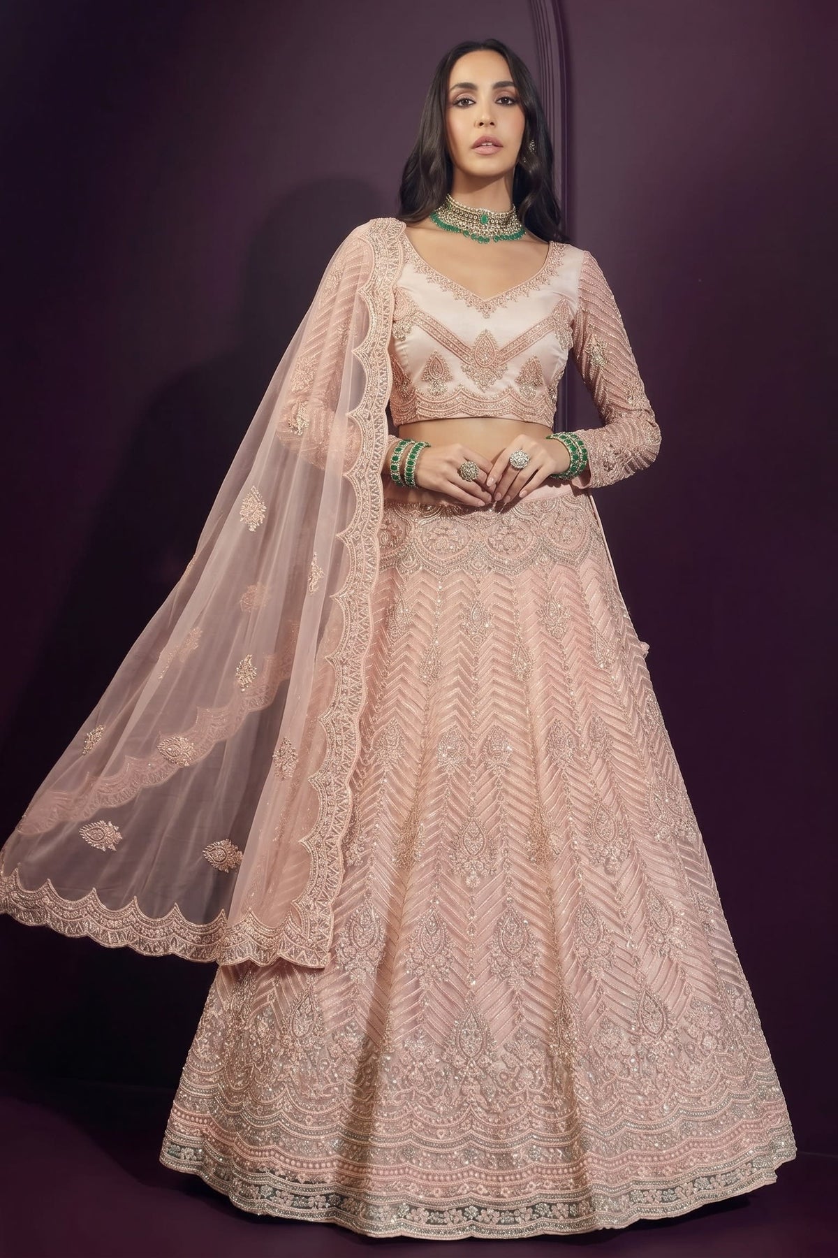 Pale peach lehenga choli for sangeet in net with hand-worked embroidery, long-sleeve choli and dupatta held out to show the sheer drape.