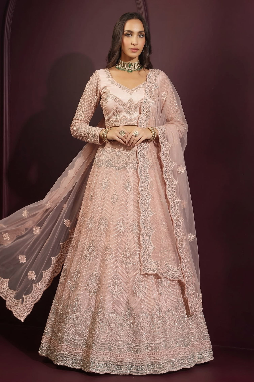 Front view of a pale peach reception lehenga with all-over hand embroidery on net, long-sleeve choli and flowing sheer dupatta.