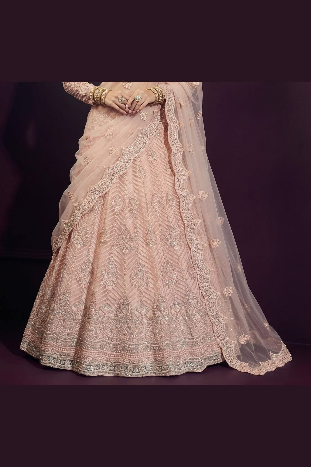 Close-up from waist down of the pale peach sangeet lehenga choli skirt showing dense hand-worked embroidery across the net fabric.