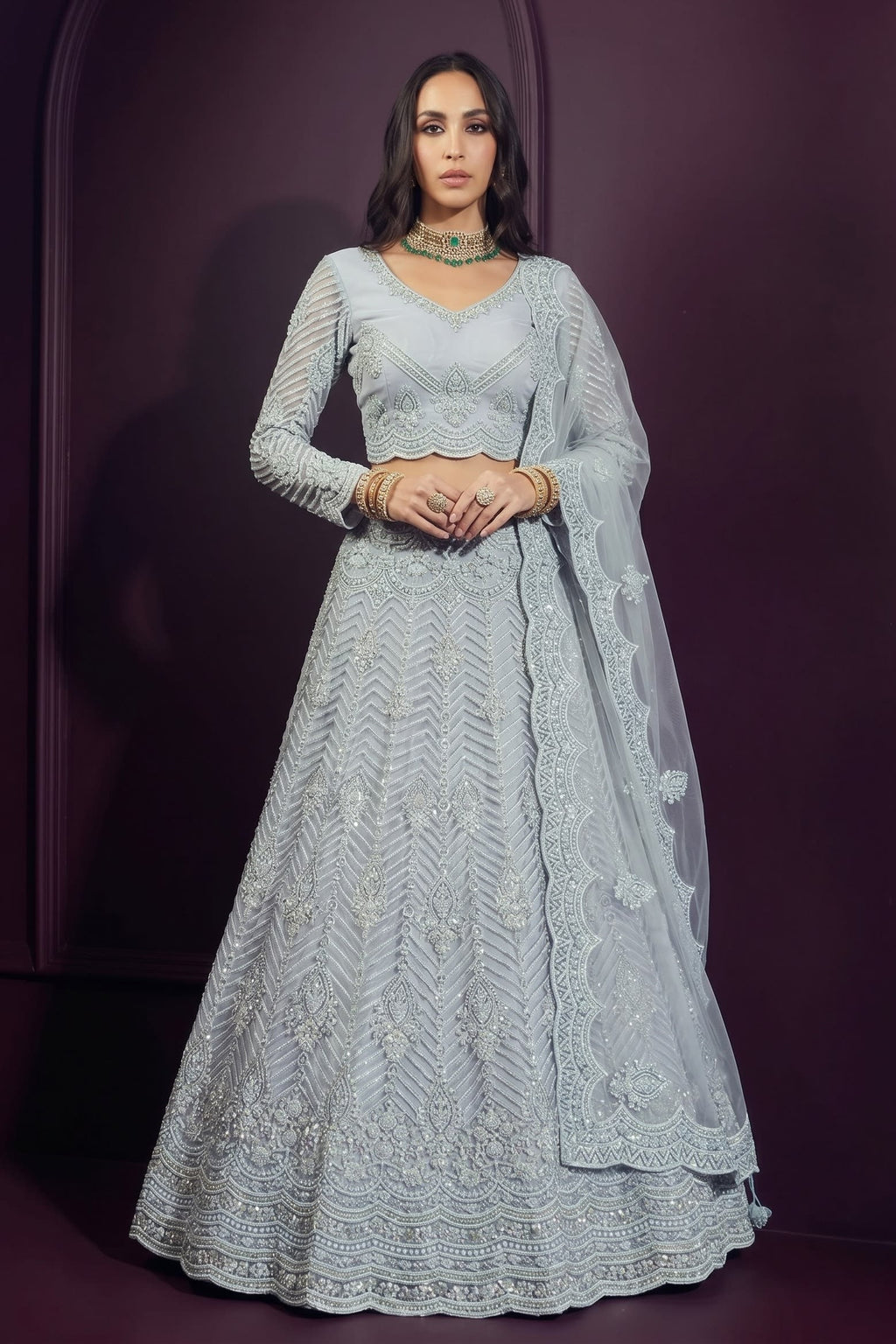 Model wearing a bluish grey reception lehenga with a long-sleeve embroidered choli, flared net skirt and sheer dupatta on one shoulder.