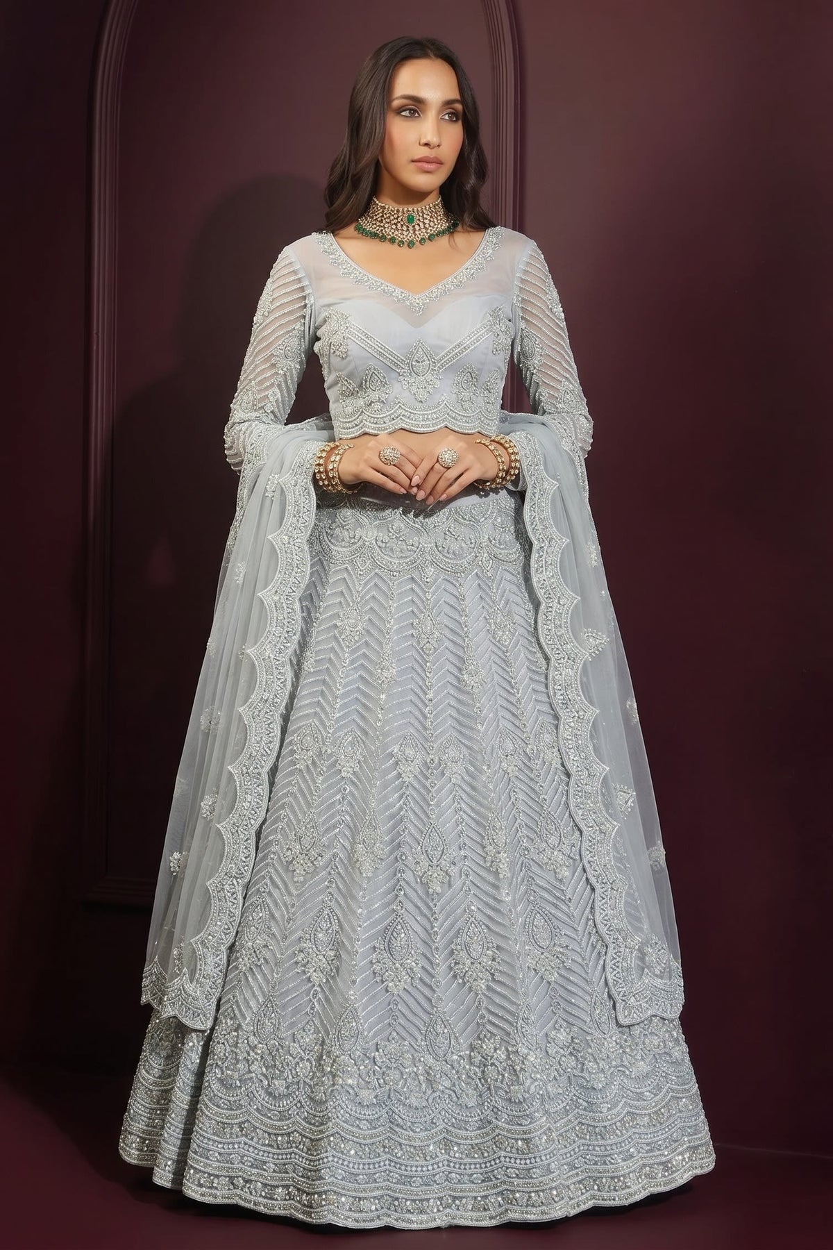 Front view of a bluish grey lehenga choli for wedding in net with hand-worked embroidery, long-sleeve blouse and dupatta on both shoulders.