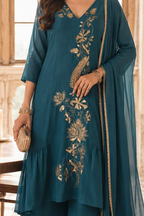 A woman wearing a teal ethnic kurta with embroidery and a matching sheer dupatta, holding a woven clutch in a softly lit indoor setting.