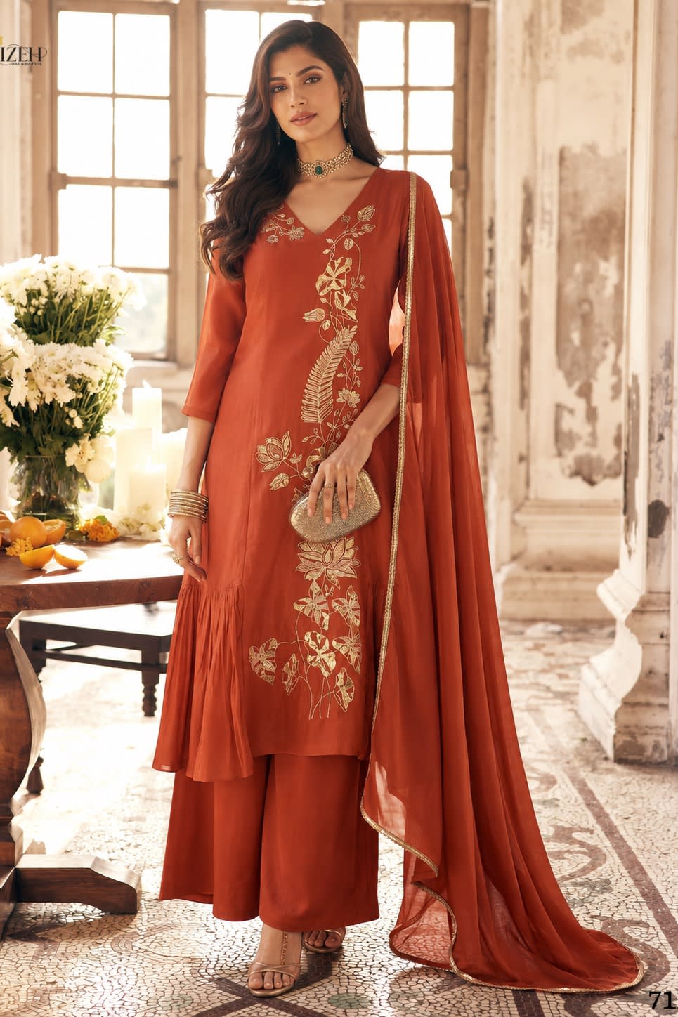 Full-length front view of rust festive wear for women, an A-line pleated kurta with pant, gold zari and sequin work and net dupatta.