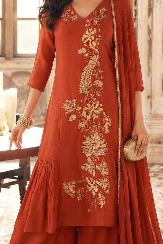 A woman models a rust-orange kurta suit with embroidery, featuring a matching dupatta 